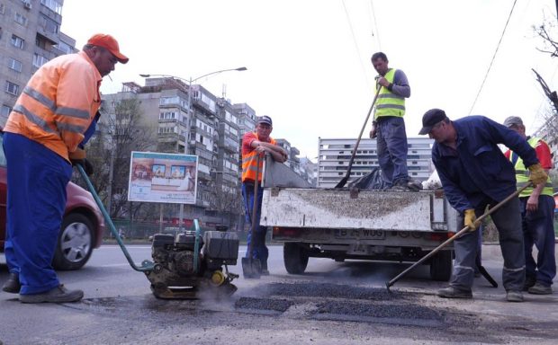 Cum acoperă muncitorii o groapă de pe bulevardul Iuliu Maniu. fac treabă cu țigara în gură