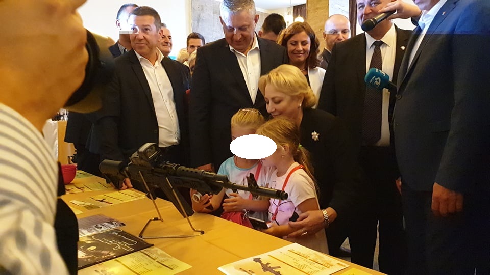 Dăncilă s-a fotografiat cu două fetițe în fața unei arme de asalt, la standul Fabricii de Arme din Cugir