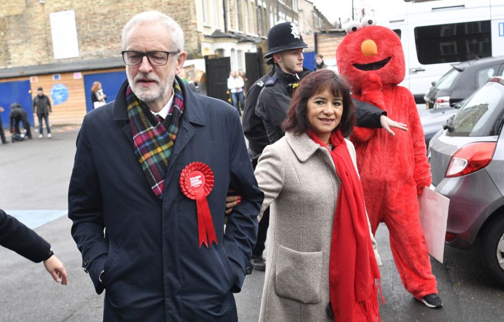 Jeremy Corbyn, alături de soția sa și de un protestatar îmbrăcat în costumul personajului Elmo, din Sesame Street, la secția de votare FOTO: EPA
