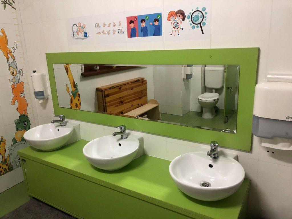 Baia dintr-o grădiniță privată din Craiova. Deasupra chiuvetelor sunt desene care le arată copiilor cum să se spele corect pe mâini
