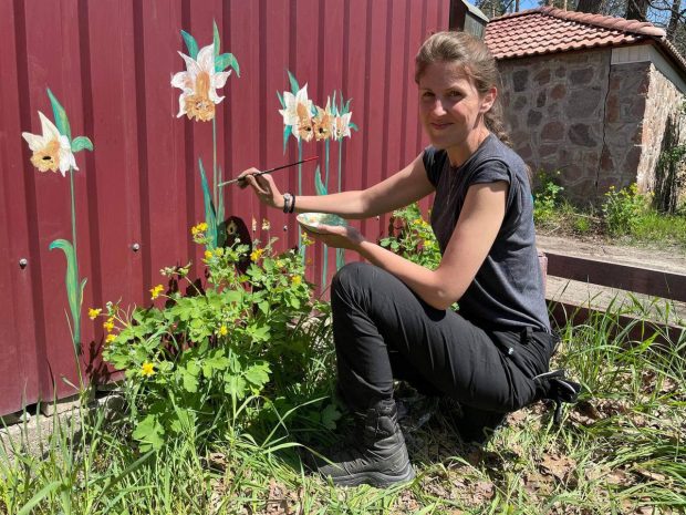Artă din gloanțe. Un artist plastic desenează flori peste urmele lăsate de cartușe în gardurile din Bucha