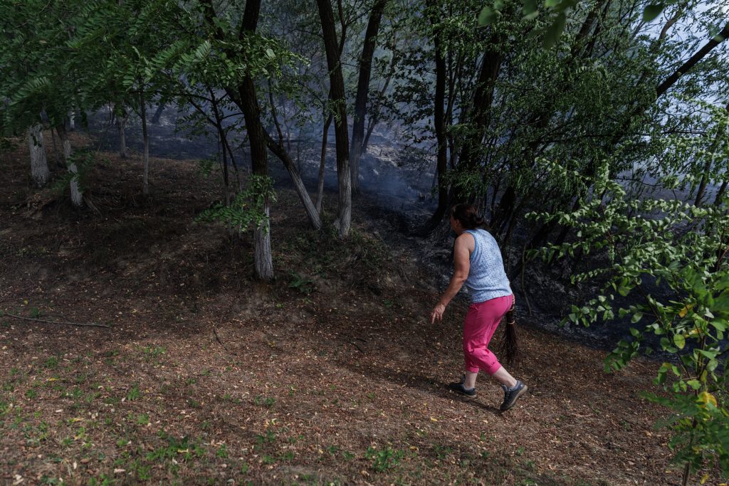 12 o femei cu un manunchi de crengi se apropie de zona in flacari