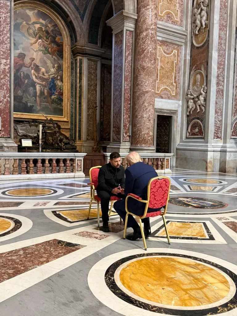 Volodimir Zelenski și Donald Trump față în față, așezați de două scaune, în interiorul Bazilicii Sf.Petru din Vatican. Trump poartă un costum albastru închis, iar Zelenski este îmbrăcat în negru - 26 aprilie 2025