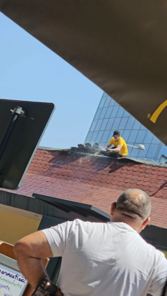 Imagine cu angajatul McDonald's Buzești urcat pe acoperiș, încercând să stingă incendiul