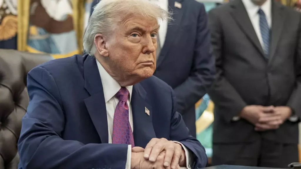 Președintele american Donald Trump, îmbrăcat la costum, stă cu mâinile una peste alta, pe masă, la biroul din Casa Albă