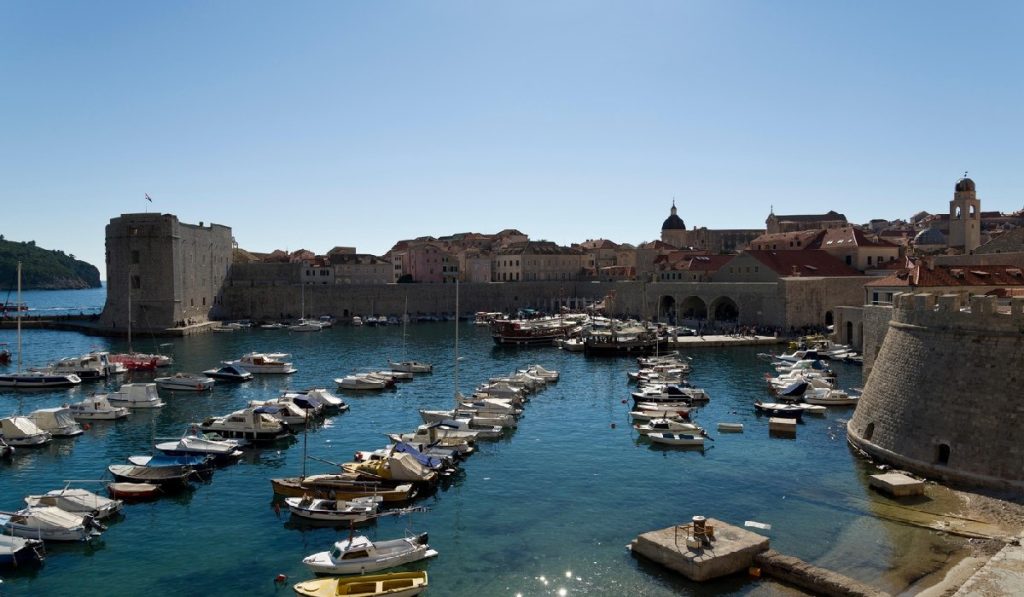 Vedere asupra portului din Dubrovnik, Croația. Muzeul maritim, zidurile orașului și cupolele bisericilor. În prim-plan se află bărci mici.
