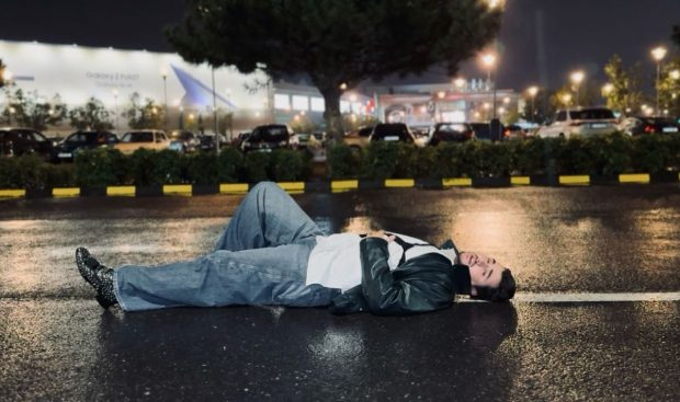 Cine este artistul filmat noaptea întins pe asfalt, în mijlocul ploii: „Scenă de film noir”