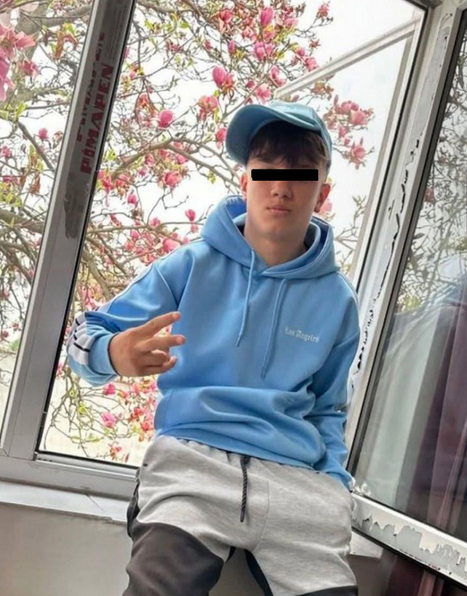 Un tanar in hanorac bleu, cu sapca sta pe pervazul unei ferestre si face semnul victoriei