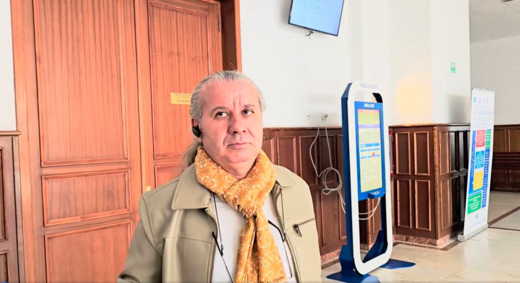 Un barbat in geaca bej cu un fular galben la gat iese dintr-o sala de judecata