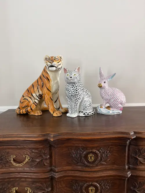 Un tigru, o pisică și un iepure de porțelan, expuse pe un obiect de mobilier